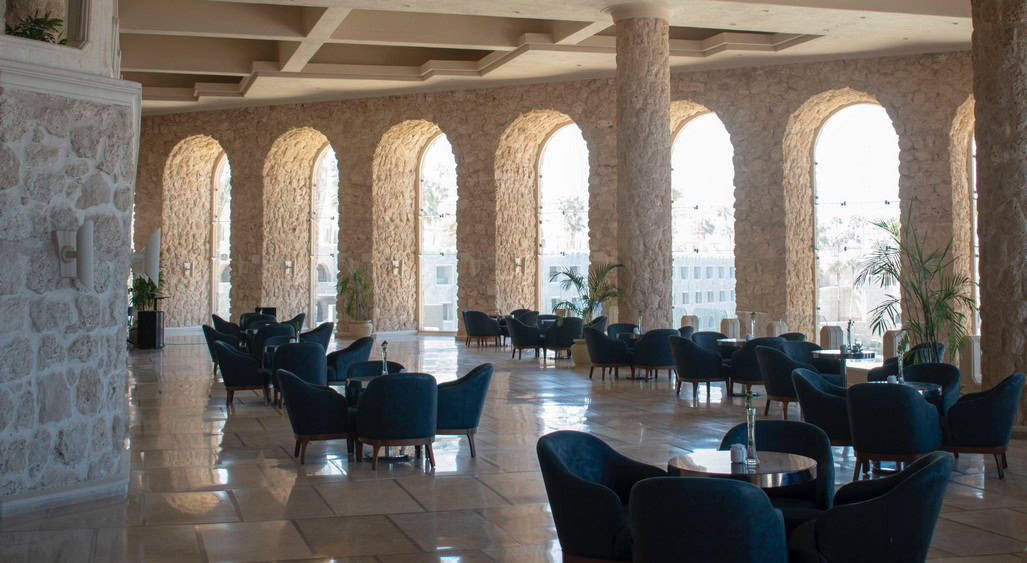 Moderno espacio de oficinas y áreas comerciales con amplios arcos de piedra y mobiliario elegante en un entorno luminoso y sofisticado.