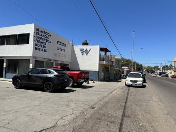 Alt text: Fachada de edificio de bienes raíces comerciales con señalización de servicios de alineación, balanceo, suspensión, frenos y m)u00f3viles, en una calle de ciudad.