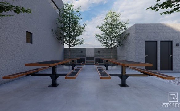 Antiguo patio con mesas y bancos de madera para espacios de reuniones o socialización, con árboles y muro de fachada moderna en un entorno urbano.