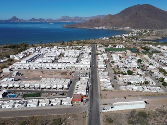 Viviendas residenciales en un desarrollo urbanístico cerca del mar en Fompo bienes raíces comerciales, vista aérea del vecindario en una zona costera con montañas de fondo.