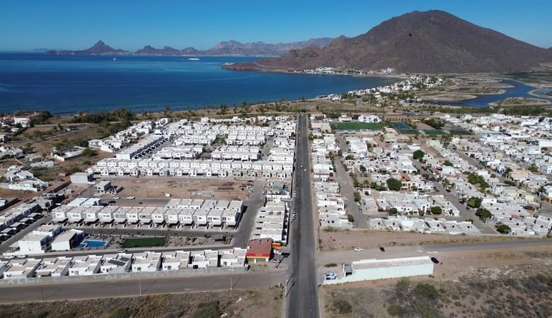 Viviendas residenciales en un desarrollo urbanístico cerca del mar en Fompo bienes raíces comerciales, vista aérea del vecindario en una zona costera con montañas de fondo.