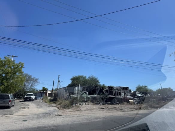 Vehículo de carga destruido en un terreno con árboles y cables eléctricos bajo cielo despejado, imagen de bienes raíces comerciales en un entorno industrial.