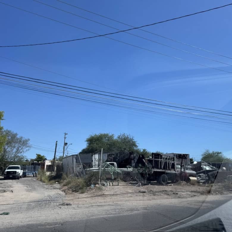 Vehículo de carga destruido en un terreno con árboles y cables eléctricos bajo cielo despejado, imagen de bienes raíces comerciales en un entorno industrial.
