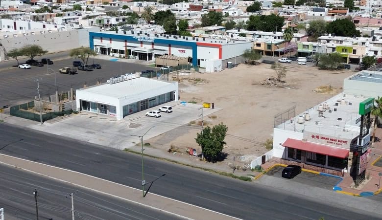 Alt text: Terreno comercial en venta en una zona urbana con edificios cercanos y fácil acceso vial.