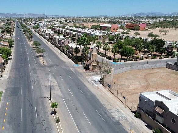 Vista aérea de una calle principal en una zona industrial con espacios comerciales y residenciales en un entorno árido, ideal para inversiones en bienes raíces comerciales en áreas urbanas.
