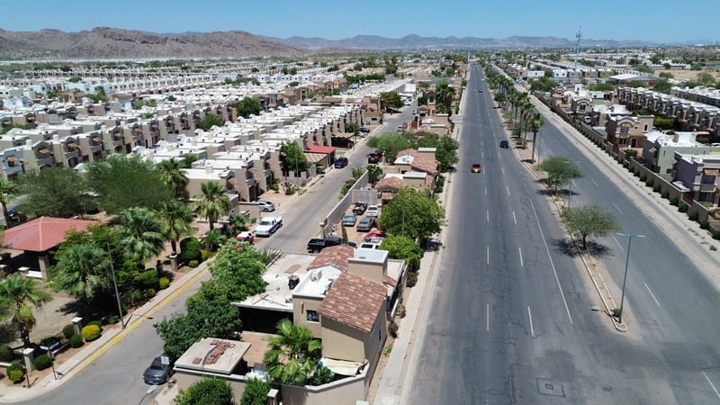 Fompo Bienes Raíces Comerciales – Vista aérea de urbanización moderna Vista aérea de una urbanización moderna con viviendas residenciales y áreas comerciales en un entorno urbano, mostrando calles amplias, áreas verdes y un paisaje montañoso al fondo.
