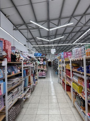 Supermercado con amplio pasillo y estanterías llenas de productos en ambos lados, con buena iluminación. Ideal para compras rápidas y cómodas en un entorno limpio y organizado.